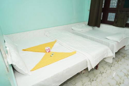 a room with two beds with white sheets and a yellow shirt at Ranjana Guesthouse in Hampi