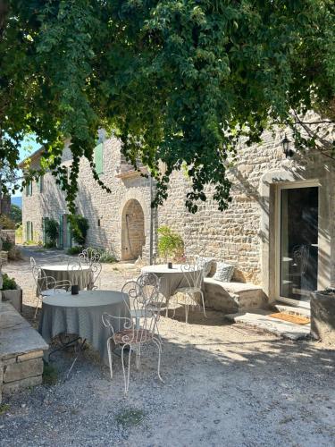 two tables and chairs under a tree in front of a building at Gîte Guillaumand in Pompignan