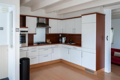 a kitchen with white cabinets and a red couch at - Het Kleine Nest - nabij het meer, strand & Keukenhof in Noordwijkerhout