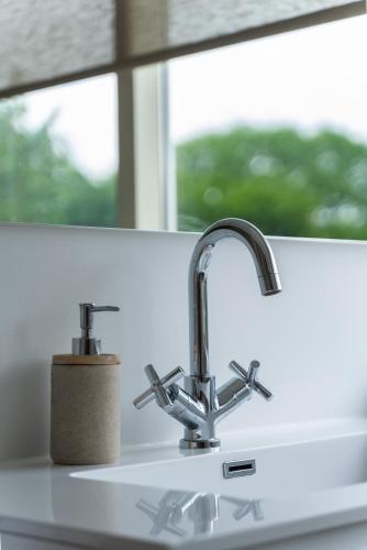 a kitchen sink with two faucets next to a window at - Het Kleine Nest - nabij het meer, strand & Keukenhof in Noordwijkerhout