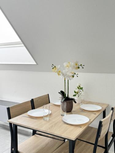 une table en bois avec deux assiettes et un vase de fleurs dans l'établissement Appartement Platanes 7 - Proche Disneyland - Parking Gratuit - Meaux, à Meaux