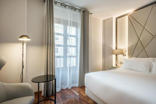 a bedroom with a bed and a chair and a window at NH Collection Salamanca Palacio de Castellanos in Salamanca