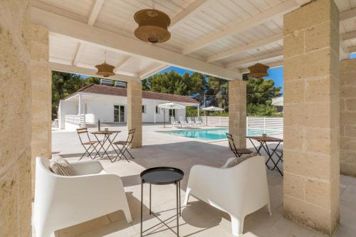 a patio with white chairs and a table and a pool at Tenuta Pietraviva by Perle di Puglia in Maruggio