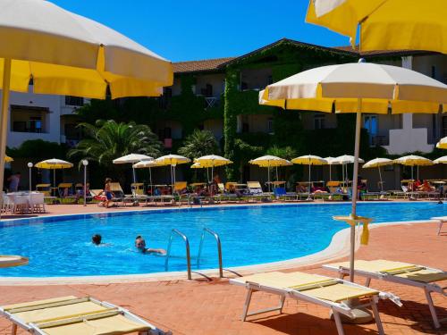 a pool with chairs and umbrellas and people in the water at Hotel La Caletta Village in La Caletta