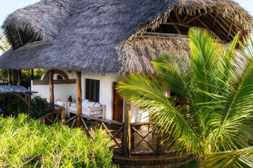 a house with a thatched roof and a palm tree at Kipepeo Residence in Malindi