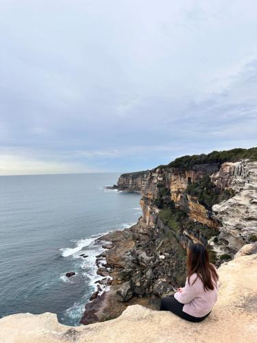 a woman sitting on a cliff looking at the ocean at Garden View Entire Self Contained Guesthouse in Engadine