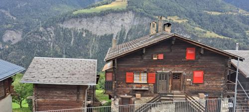 an old wooden house with red shutters in front of a mountain at Chalet Bernadette in Mörel