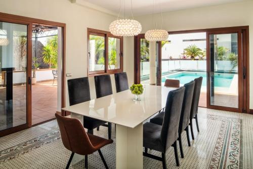 a dining room with a white table and chairs and a swimming pool at TINDAYA by Buenavilla in Puerto Calero