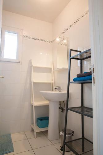 a white bathroom with a sink and a shelf at Le Pénity, studio lumineux à Carnoët in Carnoët