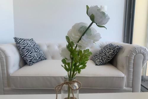 un vase avec des fleurs blanches sur une table et un canapé dans l'établissement Naturiste Cap d'Agde Héliopolis C 39, au Cap d'Agde