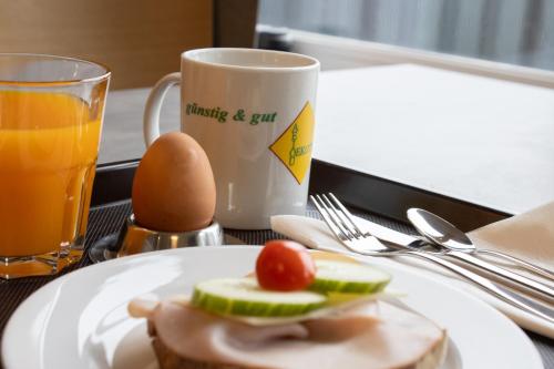 a plate with a sandwich and an egg and a cup of orange juice at OEKOTEL Graz Airport in Kalsdorf bei Graz