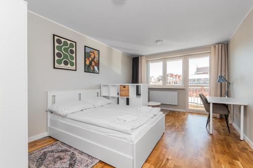 een witte slaapkamer met een bed en een bureau bij Frida by Grand Apartments in Gdańsk