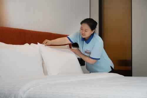 a woman standing next to a bed at Hampton by Hilton Guangzhou Baiyun Airport Cultural Tourism City in Guangzhou