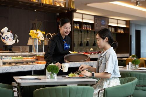 two women sitting at a table with a plate of food at Hampton by Hilton Guangzhou Baiyun Airport Cultural Tourism City in Guangzhou