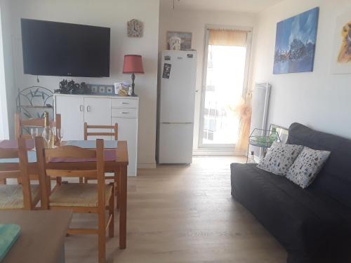 a living room with a table and a kitchen with a refrigerator at Bel appartement spacieux front de mer in Le Barcarès