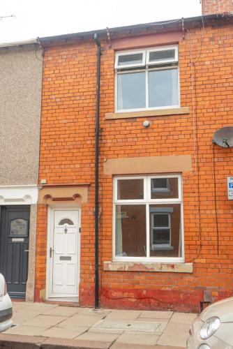 a brick building with a white door and windows at Lovely Lindisfarne in Carlisle