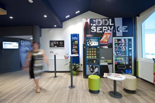 a woman walking through a room with a soda service at ibis budget Saint Paul Les Dax in Saint-Paul-lès-Dax