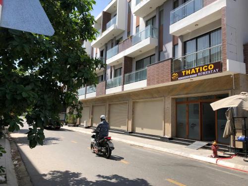 a man riding a motorcycle down a street in front of a building at Thatico Homestay in Kinh Dinh