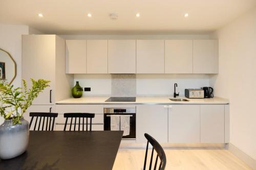 a kitchen with white cabinets and a black table and chairs at The South Wimbledon Place - Adorable 2BDR Flat with Balcony in London