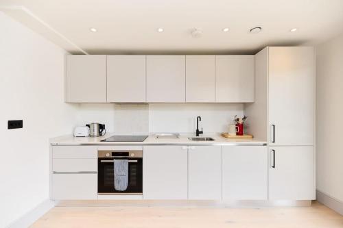 a white kitchen with white cabinets and a sink at The South Wimbledon Hideout - Fancy 1BDR Flat with Balcony in London