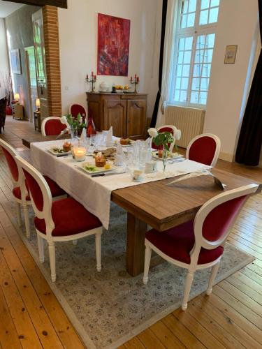 une table de salle à manger avec une nappe blanche et des chaises rouges dans l'établissement Manoir de la Gravette, Maison & Table d'Hôtes, à Montauban