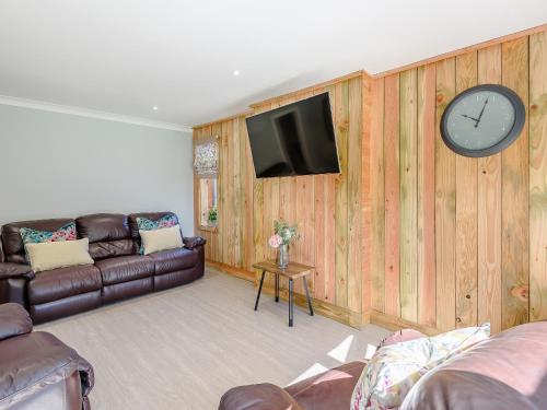 un salon avec un canapé et une horloge au mur dans l'établissement Harebell Cottage, à Addlethorpe