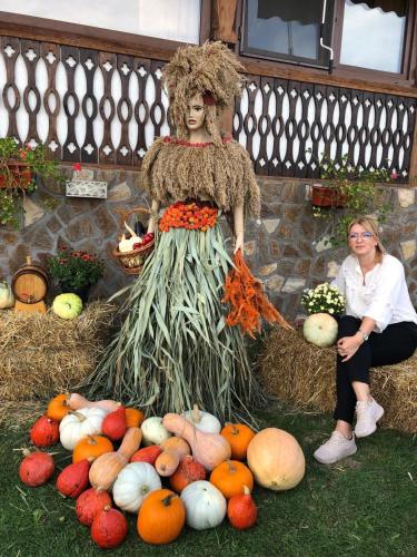 a woman sitting next to a scarecrow surrounded by fruits and vegetables at La Foisor in Vărbilău