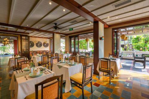 a restaurant with white tables and chairs and windows at Cozy Savvy Hoi An - The Quintessence of Exquisite Retreat in Hoi An