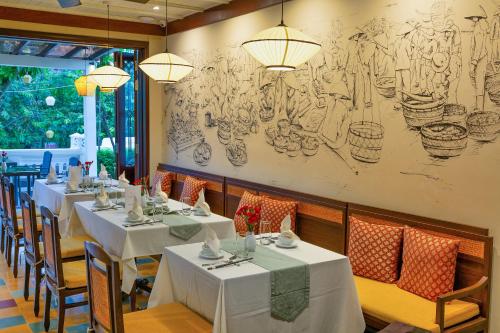a restaurant with white tables and chairs and a drawing on the wall at Cozy Savvy Hoi An - The Quintessence of Exquisite Retreat in Hoi An