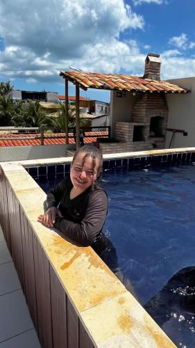 a woman leaning on a wall next to a swimming pool at Pousada Maria do Lampião Jericoacoara- Antigo Jeri Vila Mini in Jericoacoara