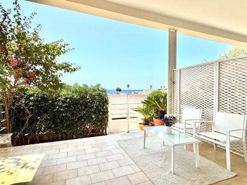 a patio with a glass table and white chairs at Villa Nauna, fronte mare con giardino e terrazzo - Marea Stays Collection in Nardò
