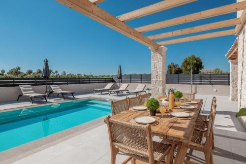 a dining table and chairs on a patio with a pool at Petra Natura Villa in Zakynthos Town