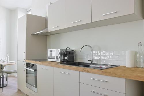 une cuisine blanche avec un évier et un micro-ondes dans l'établissement La Suite des Martyrs - Centre Ville - Elégant, à Bordeaux