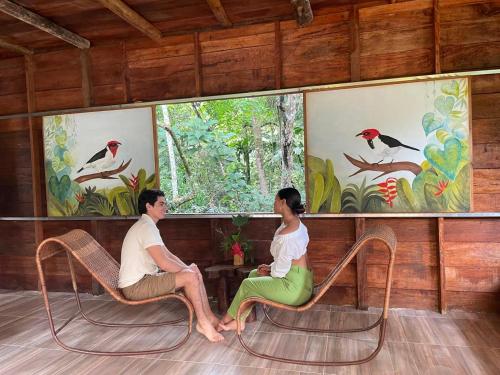 a man and woman sitting in chairs in a room with paintings at Posada Amazonia in Florencia