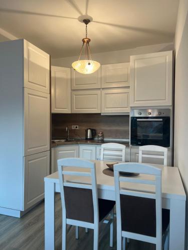 kuchnia z białymi szafkami, stołem i krzesłami w obiekcie Sunset Apartment w Prisztinie