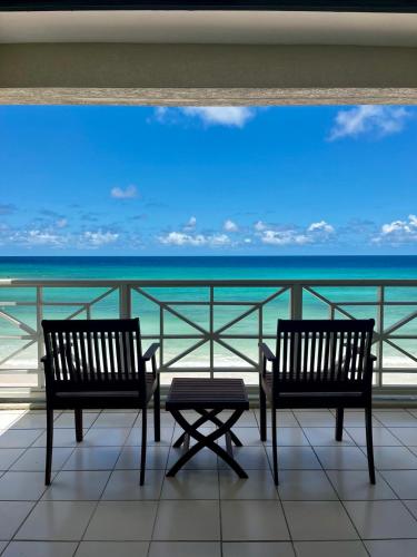 two chairs and a table on a balcony with the ocean at Hôtel Le Roy in Christ Church