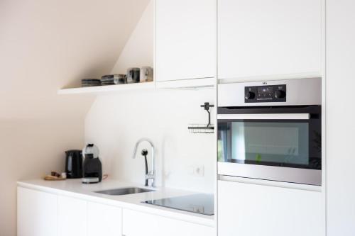 a white kitchen with a sink and a microwave at De Weldoeninge in Wingene