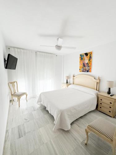 a white bedroom with a bed and a chair at Apartamento comedia in Sanlúcar de Barrameda