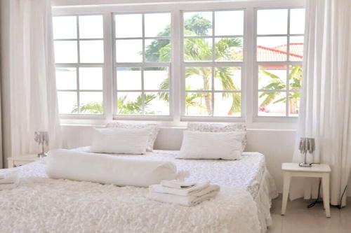 a white bedroom with two beds and windows at Group Accommodation Jan Thiel Curaçao in Willemstad