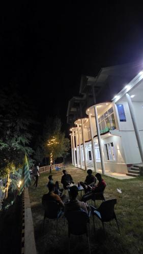 a group of people sitting in chairs outside a building at night at Ruby Lodges Upeer Neelum in Bāta