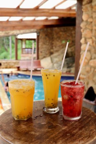 three drinks sitting on a table next to a pool at Hotel Pousada Riacho da Areia in Águas de Lindóia