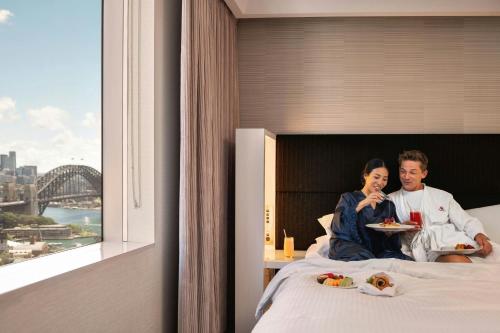 a man and woman sitting on a bed eating food at Sydney Harbour Marriott Hotel at Circular Quay in Sydney