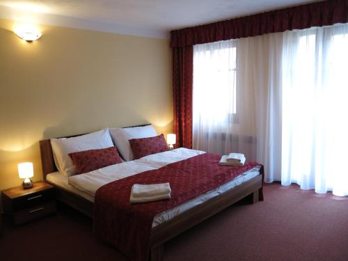 a bedroom with a large bed with red sheets and windows at Penzion Elzet in Třeboň