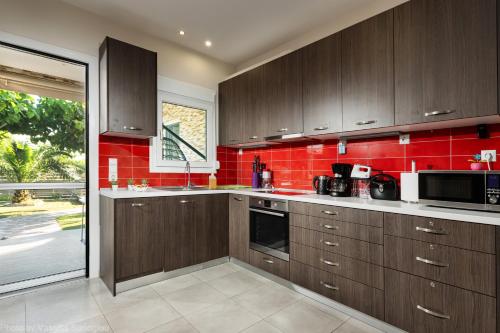 a kitchen with brown cabinets and a red wall at Costa Petra - Luxury Seaside Cottage with Garden - Vacation House for families in Greece in Néa Meságkala