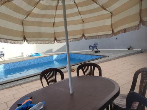 a table with an umbrella next to a swimming pool at Maison avec piscine pour famille au région de safi in Safi