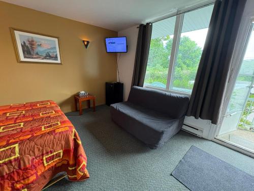 a bedroom with a bed and a chair and a window at Motel Le Voyageur in Saint-Jérôme