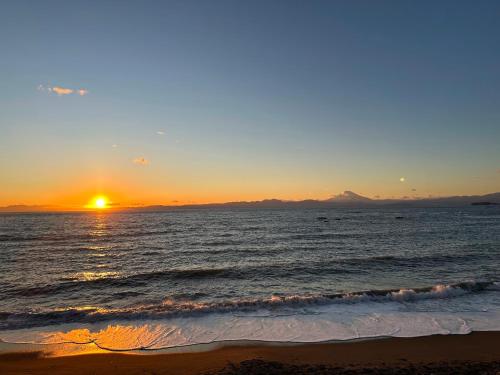 a sunset on the beach with the ocean at 葉山Yashiro - 小型犬1匹まで一緒に泊まれる一棟貸し別荘 in Hayama