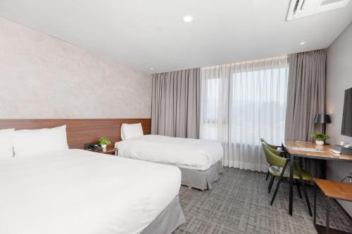 a hotel room with two beds and a desk at With Stay Jeju Hotel in Jeju