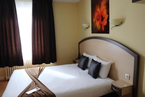 a bedroom with a white bed with black pillows at The Originals City - Hôtel Saint-Martial, Limoges Centre in Limoges