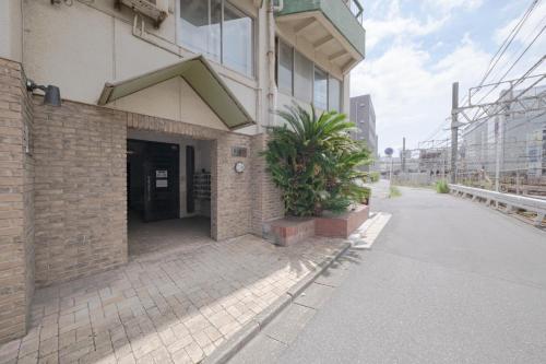 a building with a plant next to a street at 泊るHouse千葉駅1分 J - 東京ディズニーランドまで30分 線路傍騒音あり in Chiba